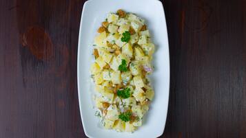 A white rectangular plate with a potato salad on a dark wooden table.