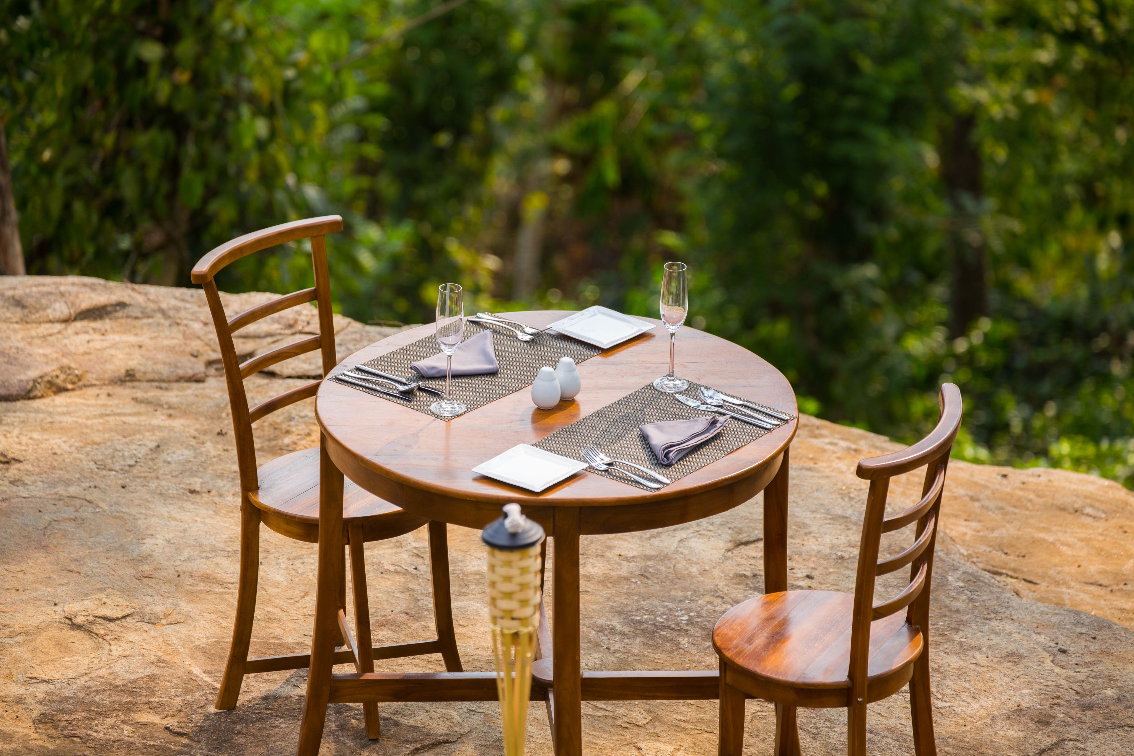 A round wooden table set for two with a placemat, cutlery, and a glass of water.