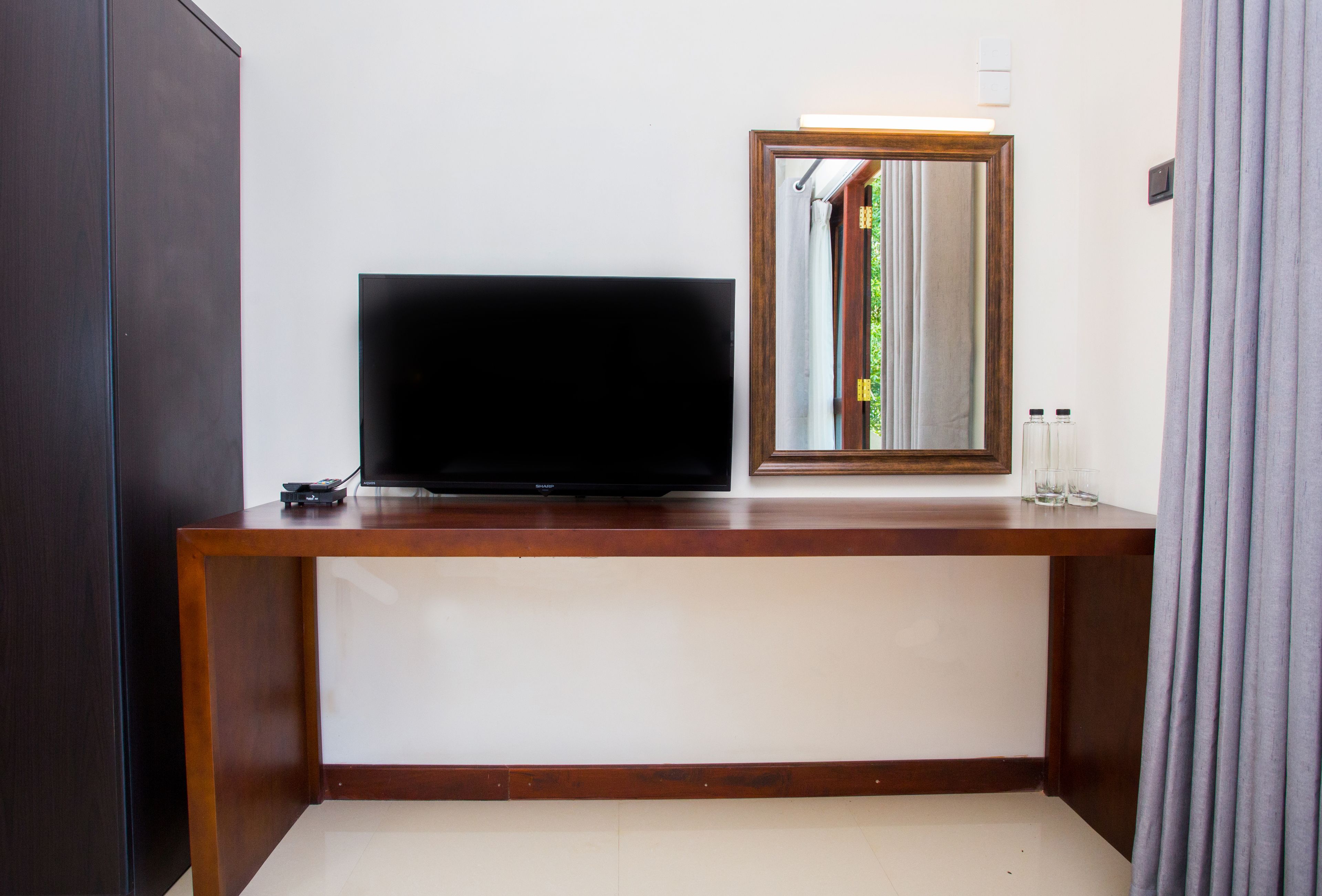 Ein Hotelzimmer mit einem Holzkonsolentisch, einem Flachbildfernseher, einem Spiegel und einer kleinen Ablage mit Pflegeprodukten.