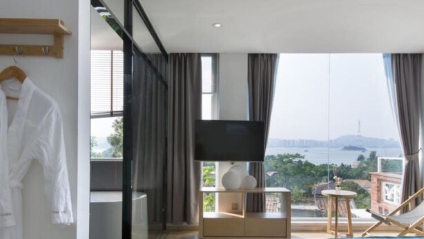 A modern hotel room with a large bed, a TV, a balcony with a view of the city, and a robe hanging on the door. - Floral Hotel Gulangyu Haiyun Garden (Xiamen)
