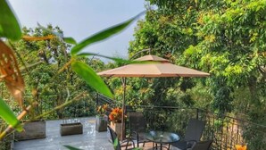 An outdoor patio with a table and chairs, surrounded by lush greenery and a large umbrella. - Floral Hotel Gulangyu Haiyun Garden (Xiamen)