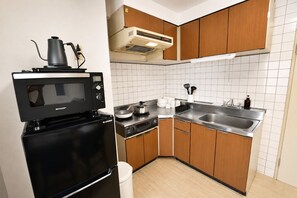 A compact kitchen with a microwave, stove, sink, and wooden cabinets. - Randor Residence Tokyo Grand (Tokyo)