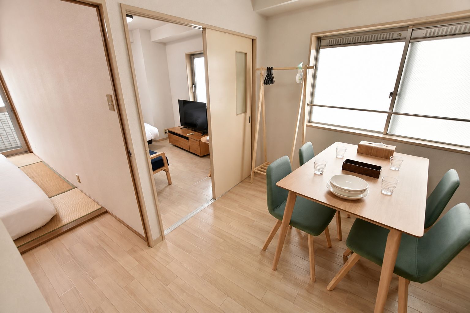 A room with a dining table, chairs, a TV, and a bed with a futon.