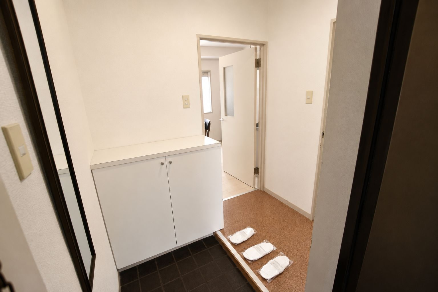 A narrow hallway with a white cabinet and a corkboard with notes on the floor.