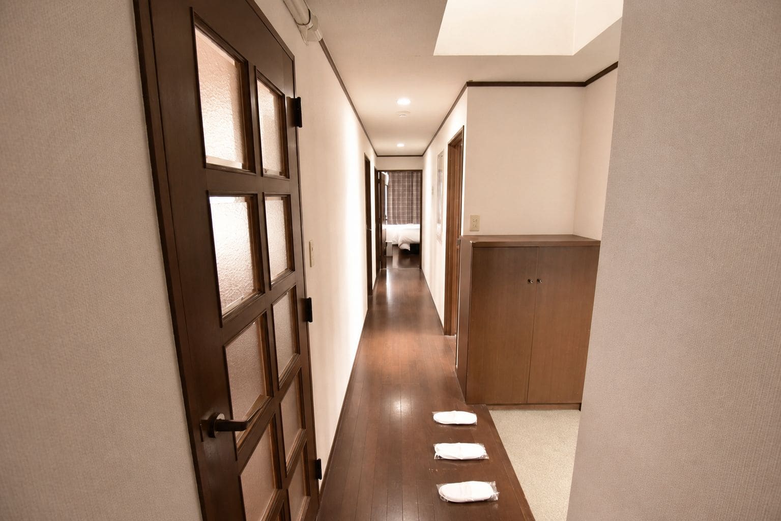 A hallway with a wooden door, a wardrobe, and a bed in the distance.
