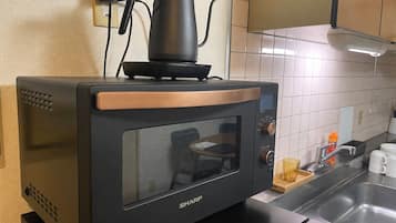 A kitchen with a built-in microwave oven, a kettle, and a sink.