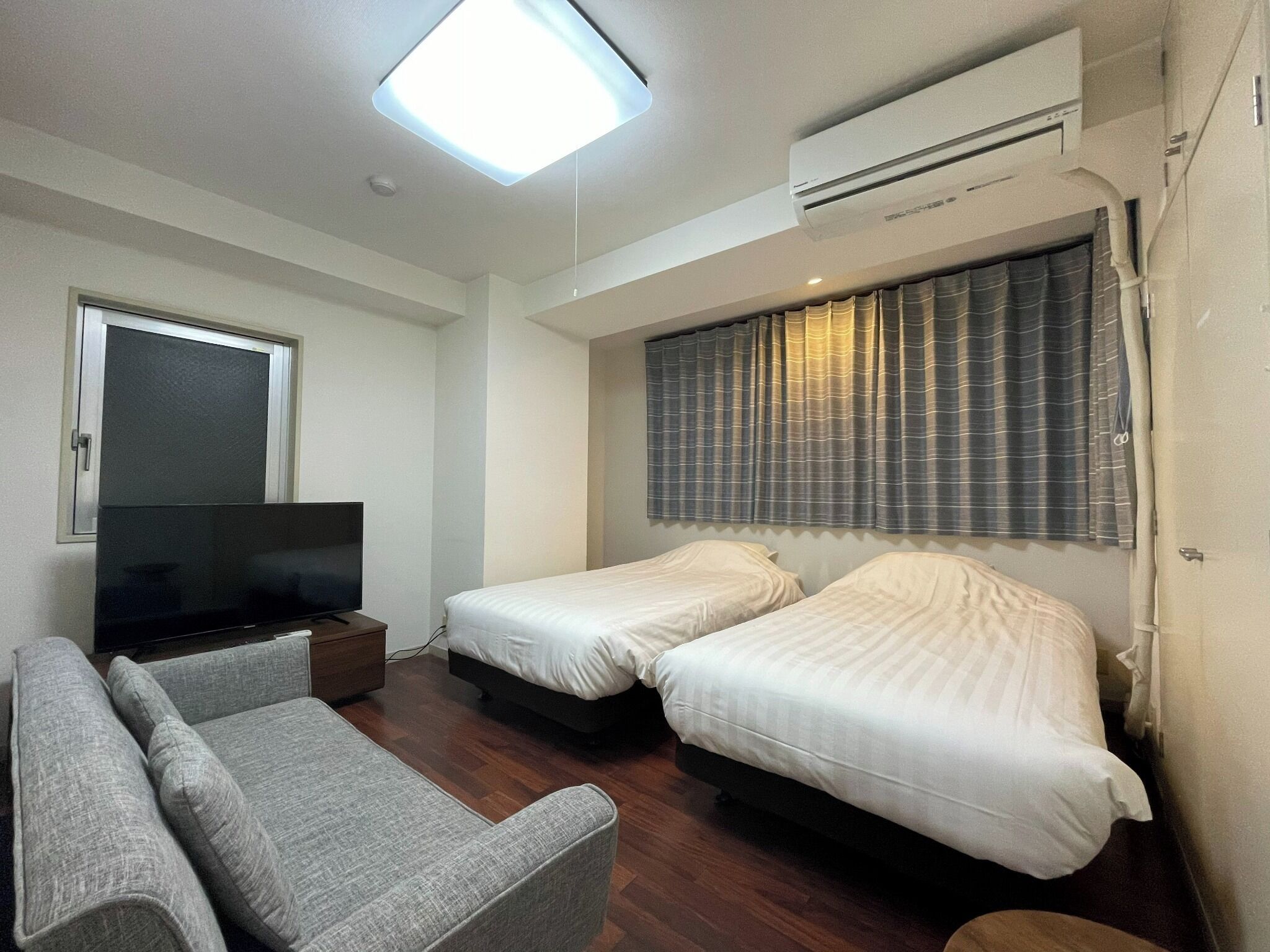 A room with two beds, a sofa, a TV, and an air conditioner.