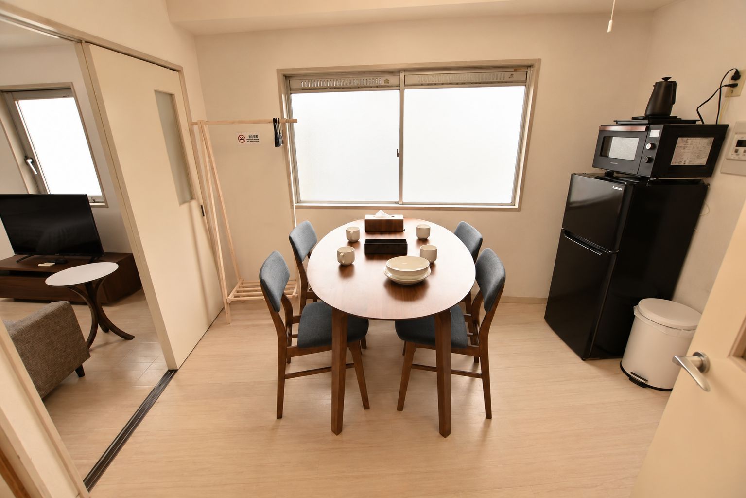 Un espacio habitable compacto con una mesa de comedor para cuatro, una zona de cocina equipada con microondas y refrigerador, y un televisor en una esquina.