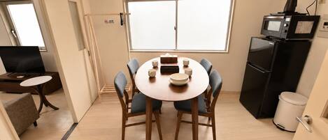 Un espace de vie compact comprenant une table à manger pour quatre personnes, un coin cuisine équipé d’un four à micro-ondes et d’un réfrigérateur, ainsi qu’un téléviseur placé dans un coin.