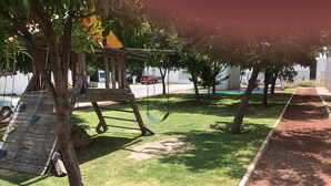 A playground with climbing structures and swings, surrounded by trees and a dirt path. - Hermosa casa completa en coto privado (Aguascalientes)