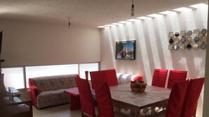 A dining area with a wooden table and red chairs, a sofa, and a wall-mounted decorative piece. - Hermosa casa completa en coto privado (Aguascalientes)