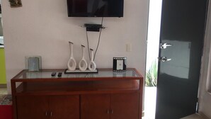 A room with a flat-screen TV mounted on the wall, a wooden cabinet with a glass top, and a door leading outside. - Hermosa casa completa en coto privado (Aguascalientes)