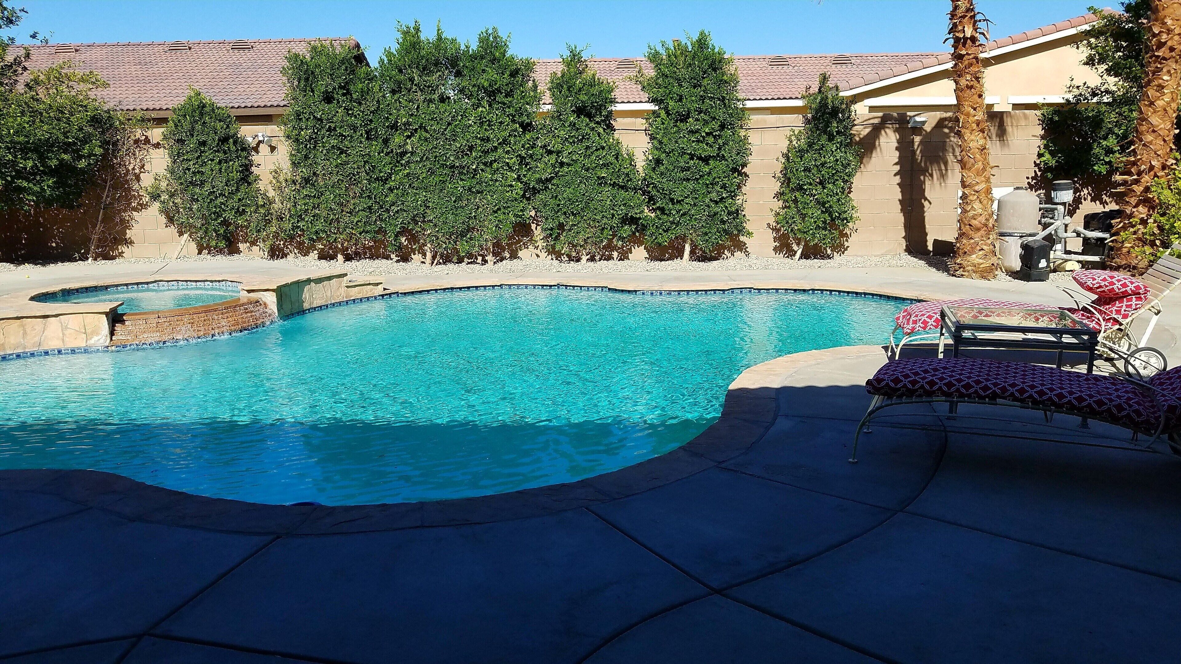 A swimming pool with a curved design, surrounded by a patio area with lounge chairs and a barbecue grill.