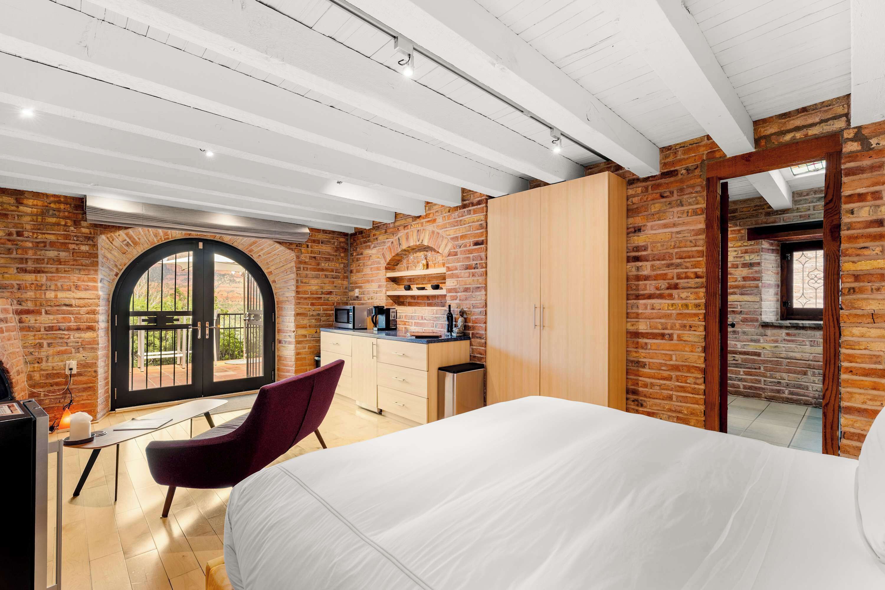 Een slaapkamer met een bed, een bureau, een stoel, een kledingkast en een keukenhoek met een magnetron.