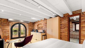 A bedroom with a bed, a desk, a chair, a wardrobe, and a kitchen area with a microwave.