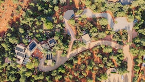 An aerial view of a residential area with winding roads, solar panels on buildings, and dense greenery.
