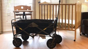 Ein Zimmer mit einem hölzernen Babybett, einem Kinderwagen und einem Fenster mit Jalousien.