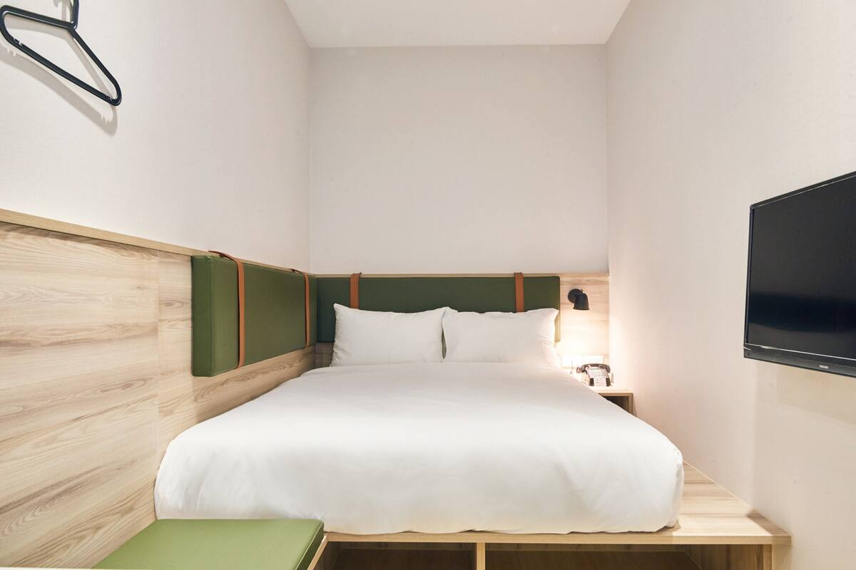A neatly arranged hotel room with a bed, a bedside table, a flat-screen TV, and a wall-mounted hanger.