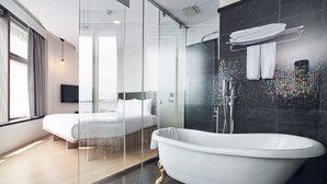 A modern hotel room with a glass-enclosed shower, a white bathtub, a bed, and a city view. - CHECKinn Express New Taipei Tamsui (New Taipei City)