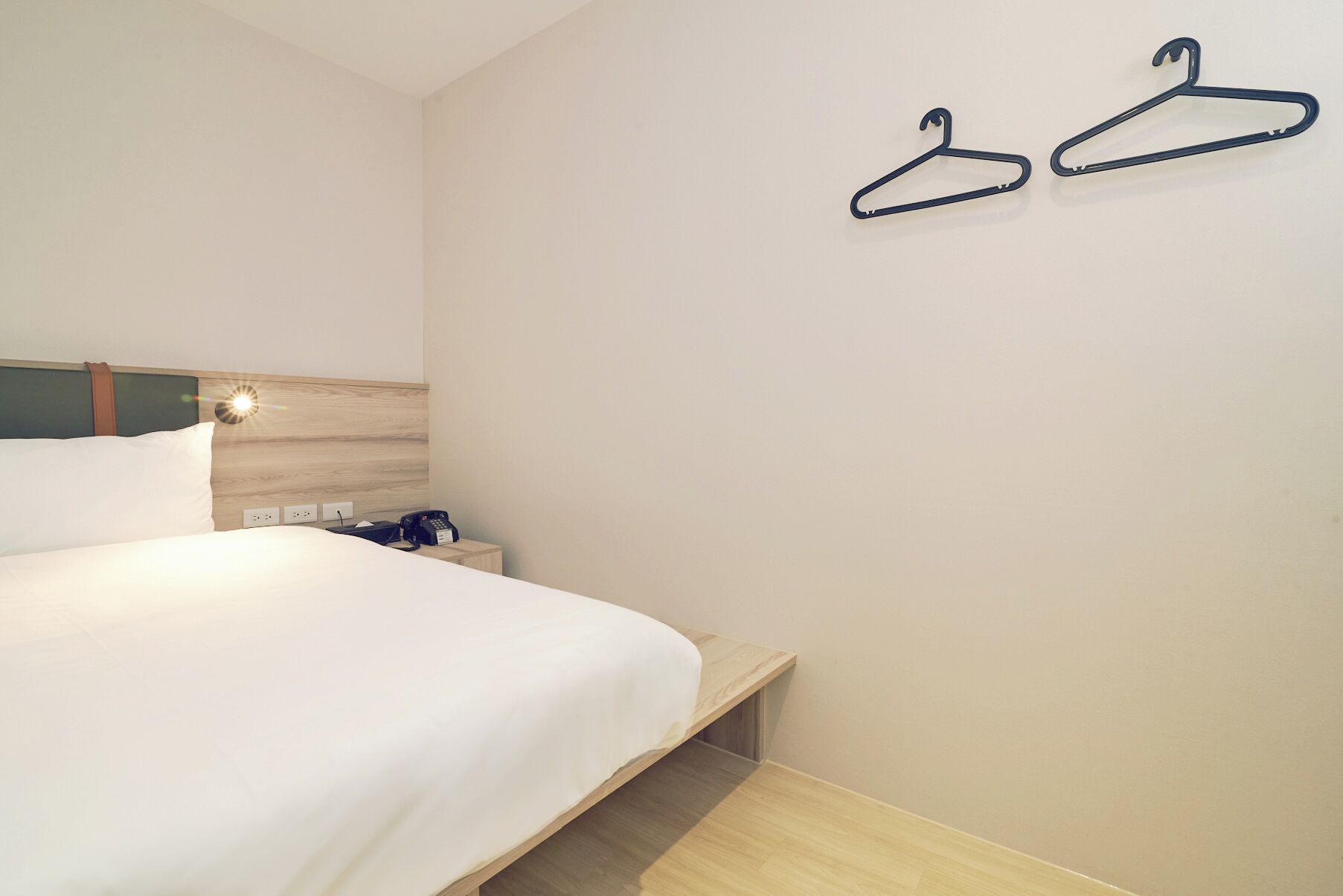 Une chambre d’hôtel comprenant un lit, une table de chevet et deux patères fixées au mur.