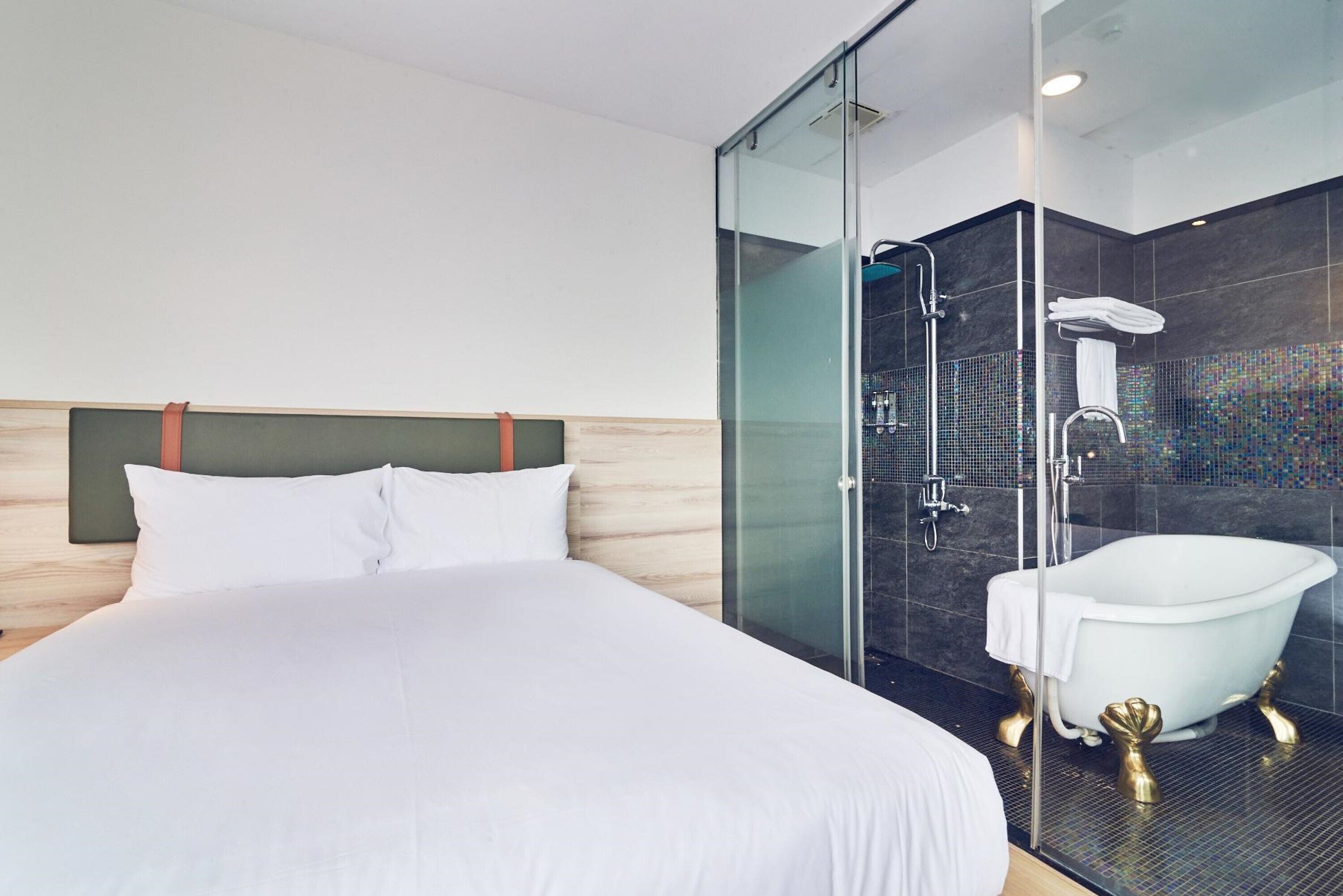 Une chambre d’hôtel moderne dotée d’un grand lit, d’une douche séparée par des parois en verre et d’une baignoire blanche classique.