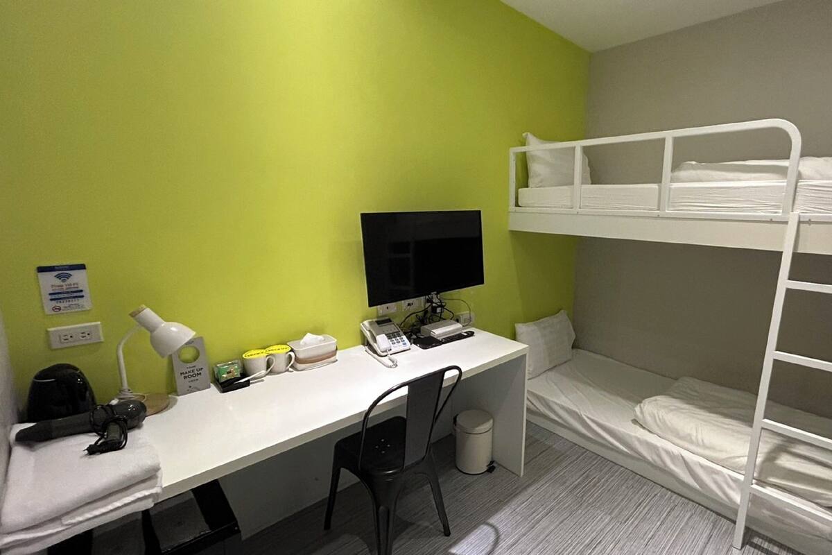 A bunk bed room with a desk, computer, and a small trash bin.