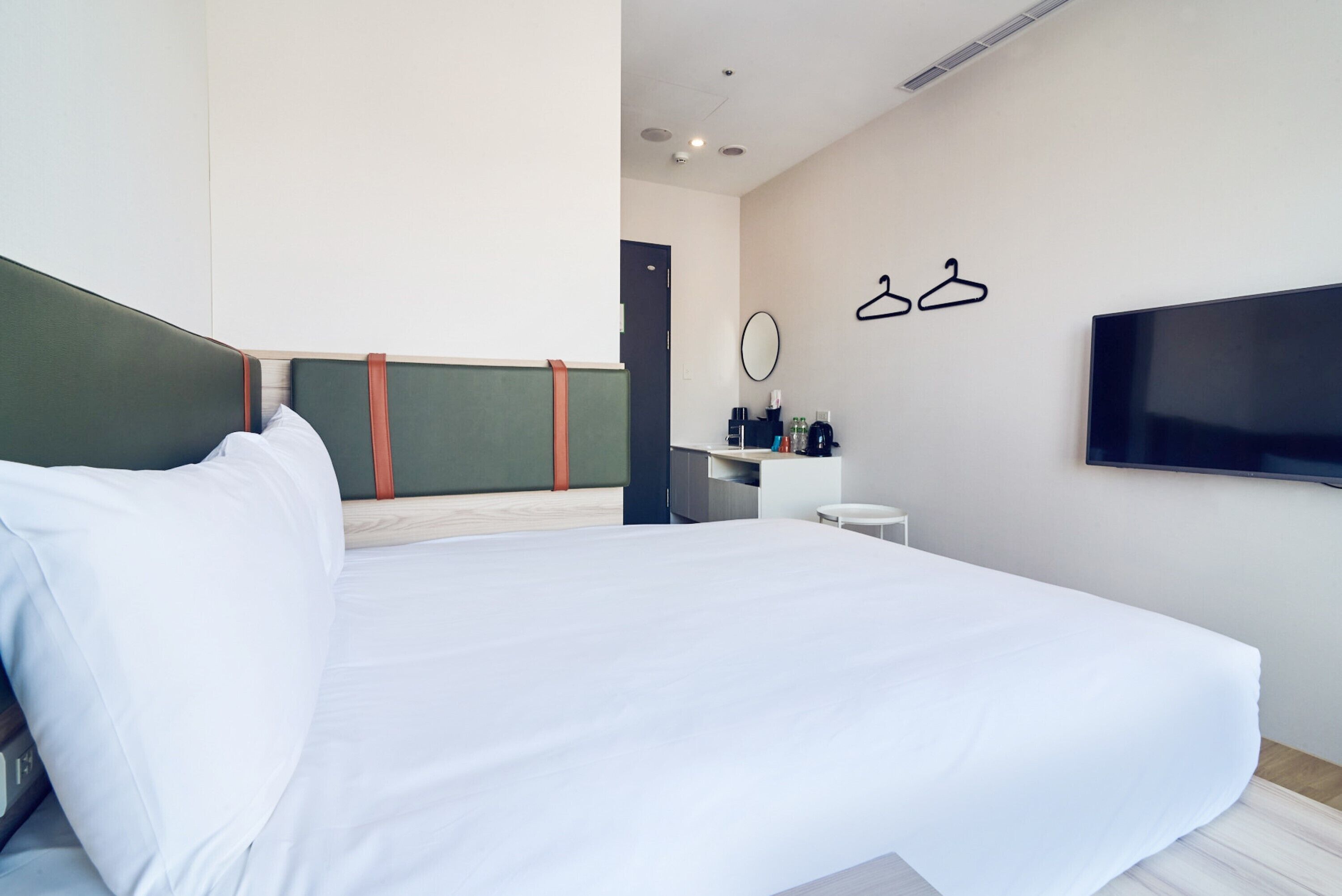 Une chambre d’hôtel moderne équipée d’un lit, d’une télévision, d’un bureau avec une chaise et d’une armoire avec un miroir.