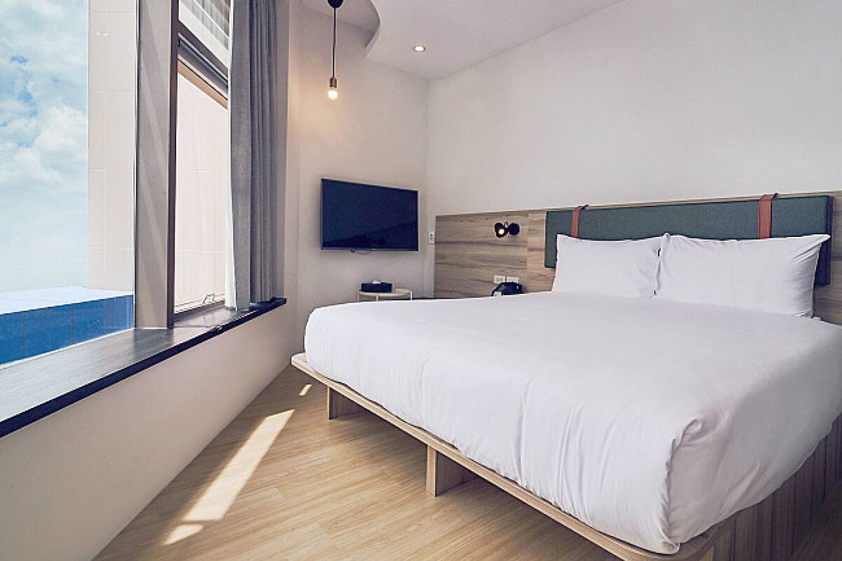 A modern hotel room with a large bed, a TV mounted on the wall, and a window with a view of the sky.