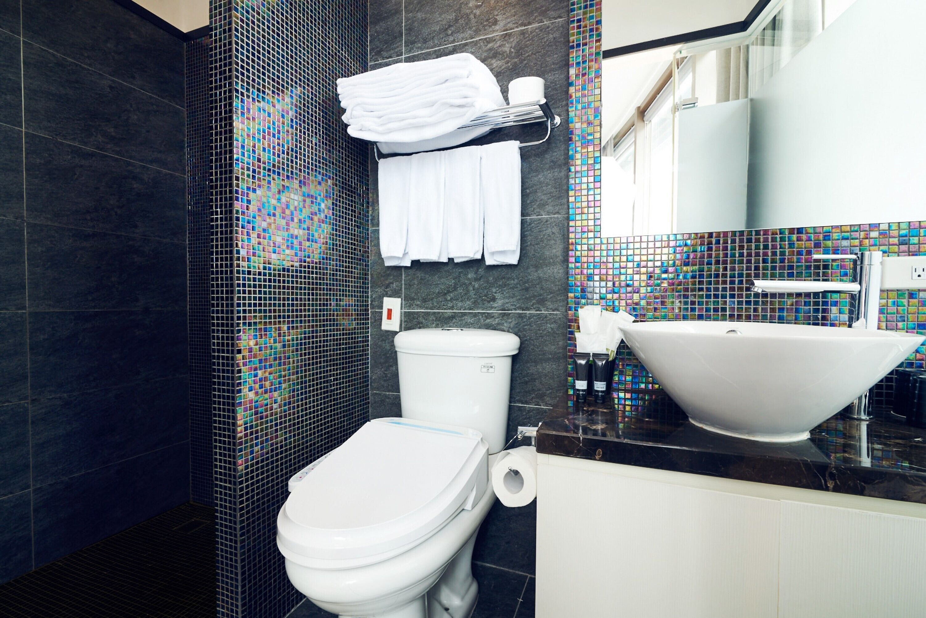 Une salle de bain moderne avec des toilettes, un lavabo et un mur recouvert de carreaux.