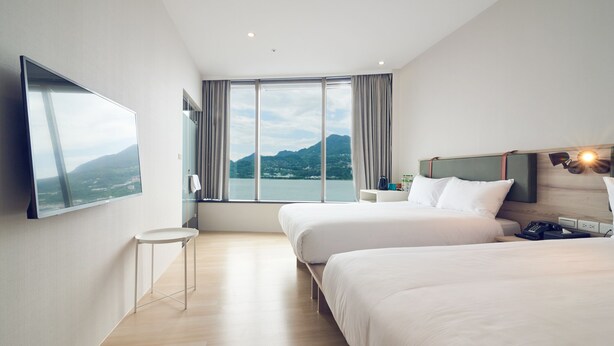 A modern hotel room with two beds, a large window with a mountain view, a flat-screen TV, and a small side table. - CHECKinn Express New Taipei Tamsui (New Taipei City)