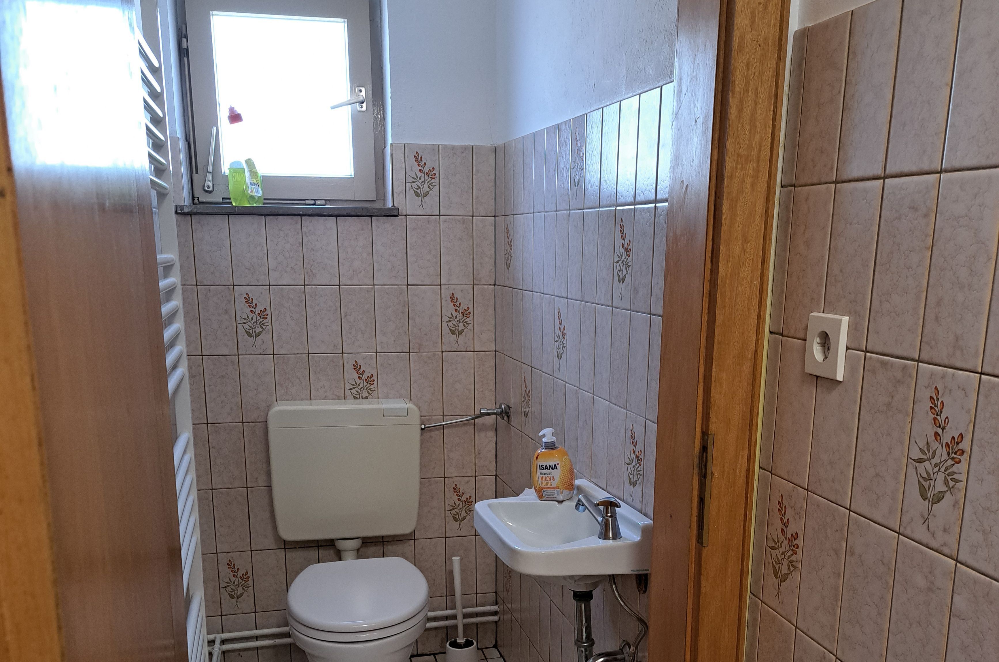 A small bathroom with a toilet, sink, and window.