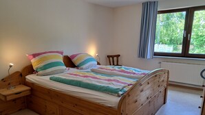 A wooden bed with a colorful striped bedspread and pillows, a bedside table with a lamp, and a window with curtains.