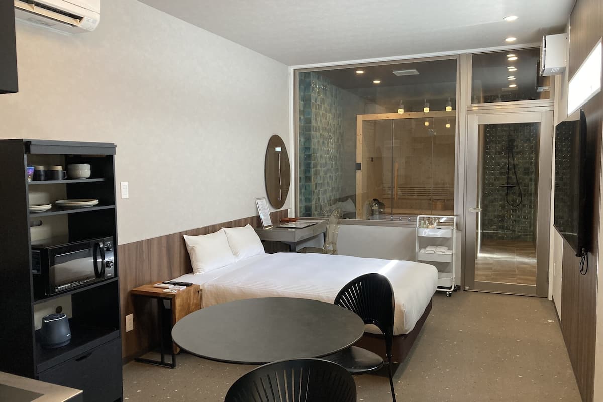 Habitación de hotel con cama, escritorio con computadora, microondas, una mesita con silla y zona de ducha de vidrio.