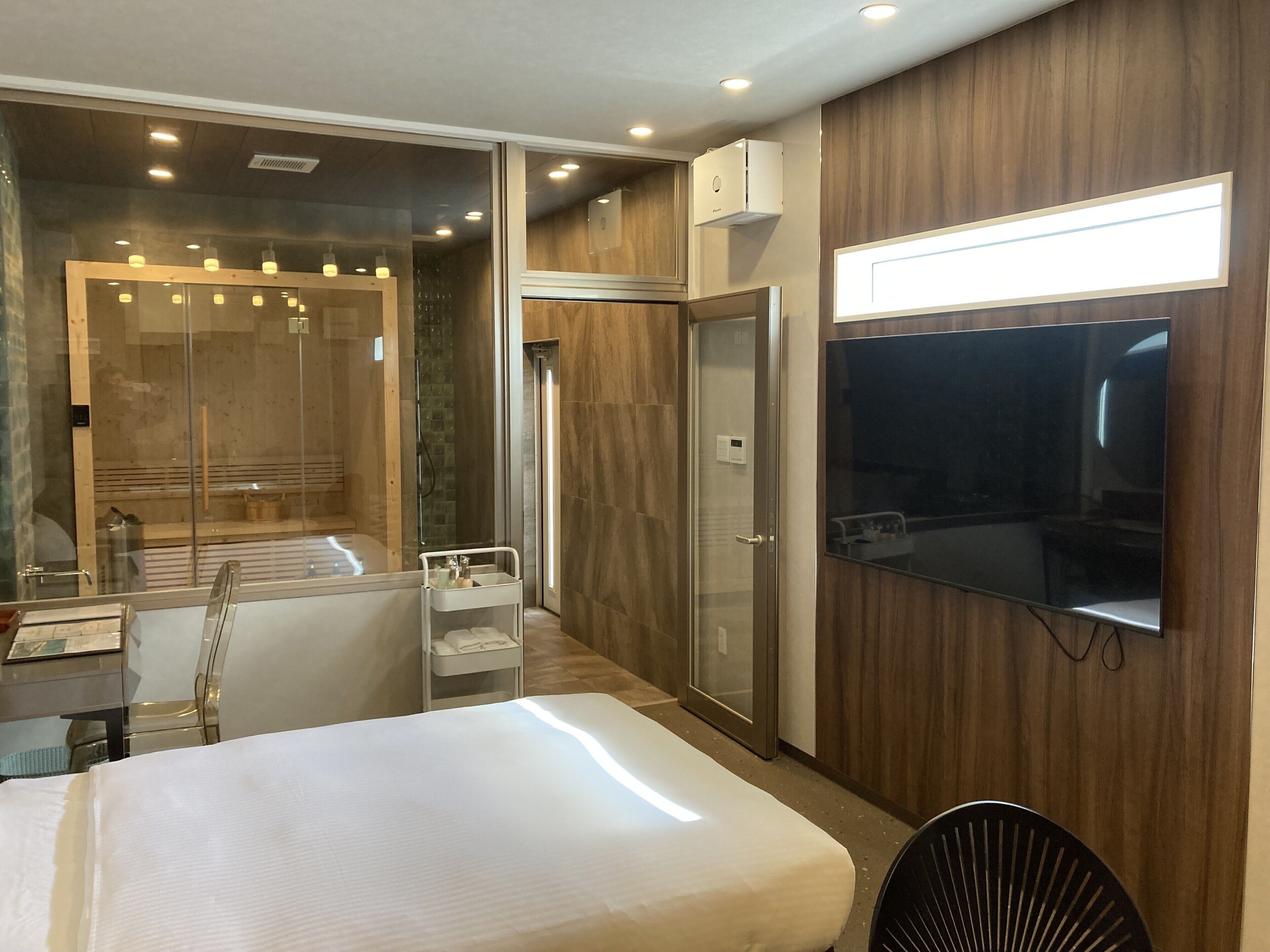Una habitación de hotel moderna con una cama grande, zona de ducha, tocador con espejo y televisor de pantalla plana montado en la pared.
