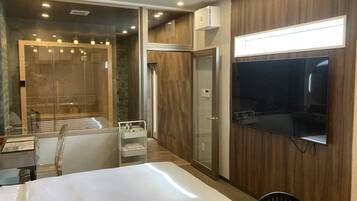 Una habitación de hotel moderna con una cama grande, zona de ducha, tocador con espejo y televisor de pantalla plana montado en la pared.