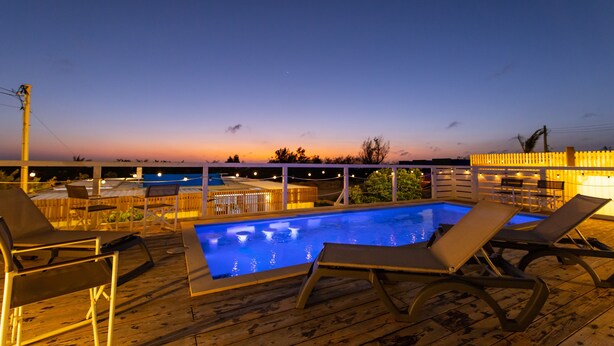 Une terrasse en bois avec une piscine, des chaises longues et des guirlandes lumineuses.