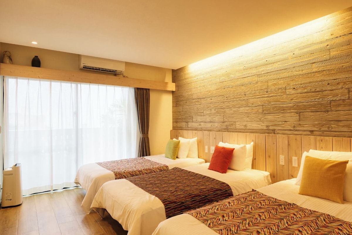 A hotel room with two beds, wooden headboard, large windows with curtains, and a visible air conditioning unit.