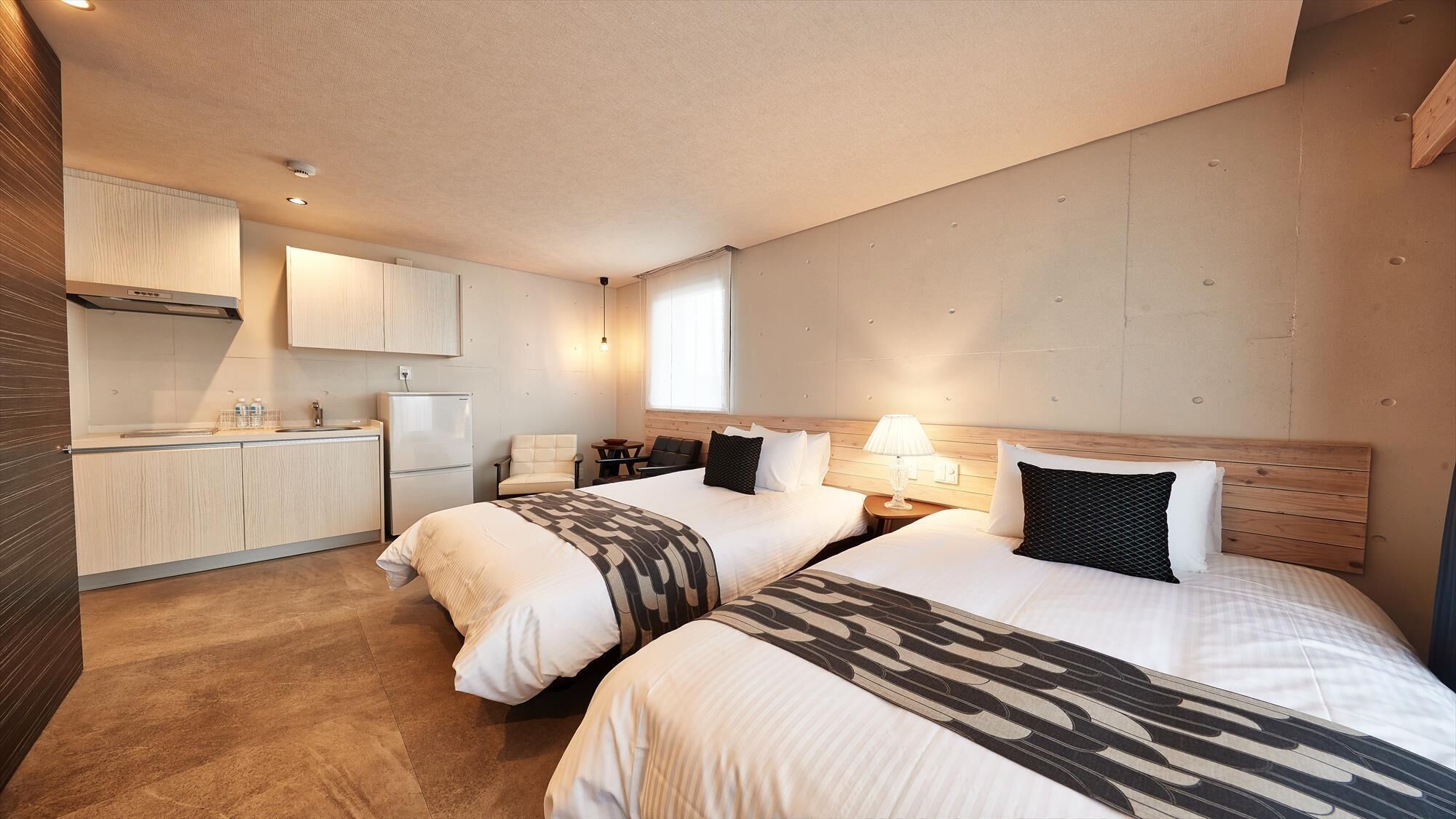 A hotel room with two beds, a kitchenette, and a large window.