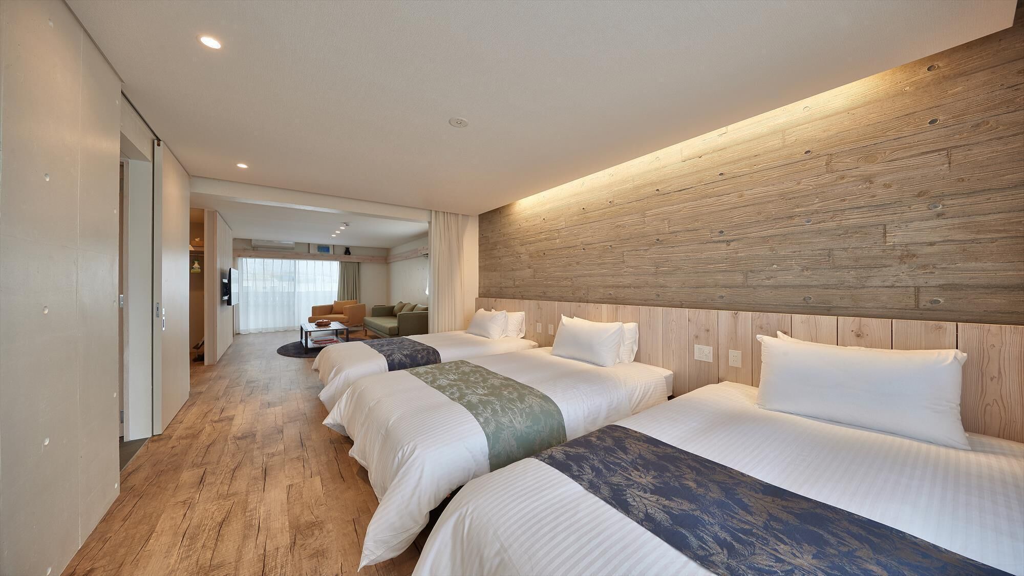 A hotel room with a wooden headboard, two beds with white bedding, a sofa, and a TV.