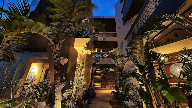 A building with a central atrium surrounded by lush tropical plants, a staircase leading to upper floors, and a bicycle parked against the wall. - Yomitan Condhotel ND (Yomitan)
