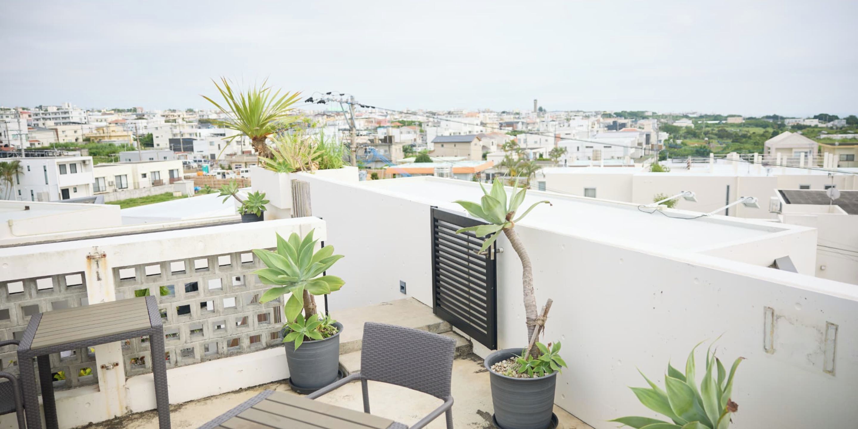 A rooftop terrace with potted plants, a chair, and a view of the cityscape.