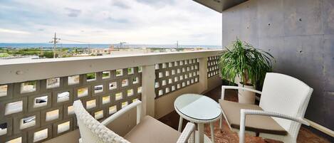 A balcony with white wicker furniture, a small table, and a potted plant.