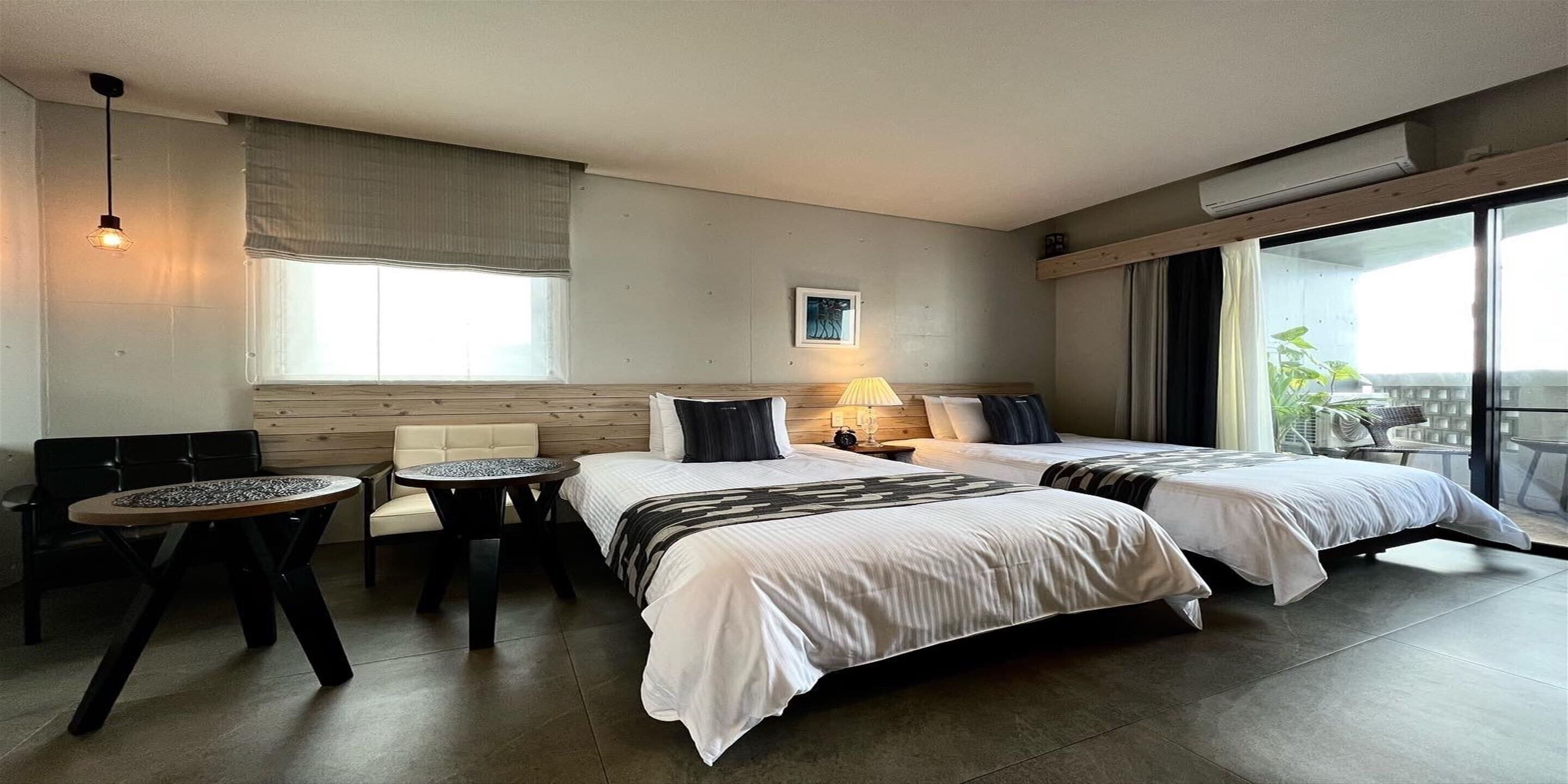 A hotel room with two beds, a small table, a sofa, and a balcony with a view.