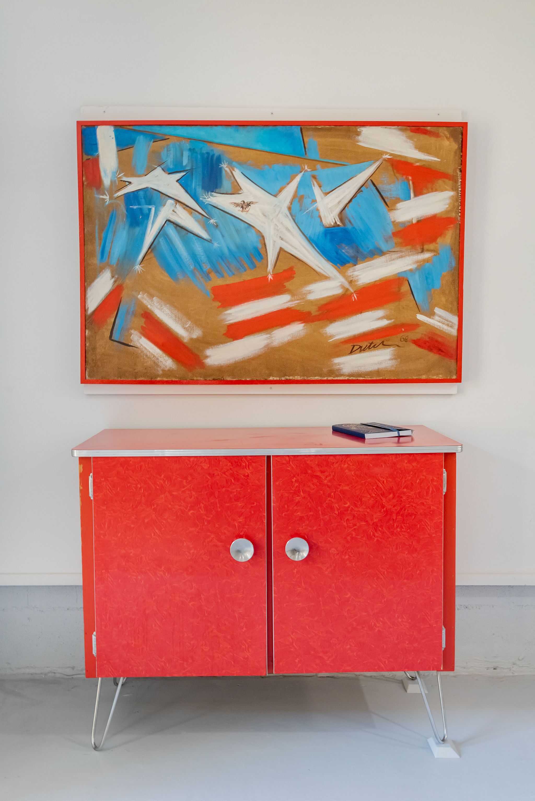 Un mueble rojo con dos cajones y un cuadro encima.
