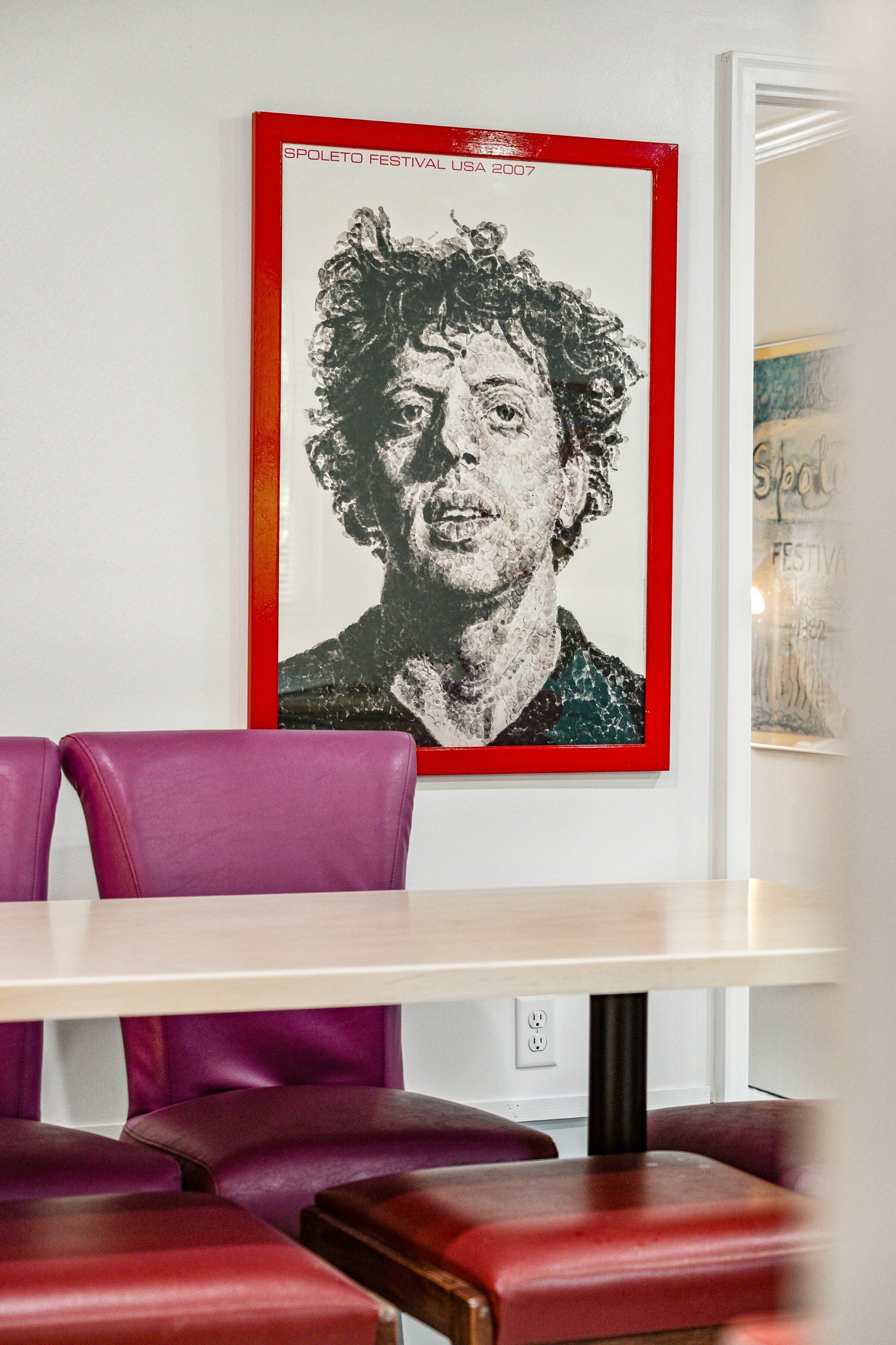 A dining area with a table and purple chairs, a framed poster on the wall, and a partial view of another poster.