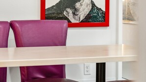A dining area with a table and purple chairs, a framed poster on the wall, and a partial view of another poster.