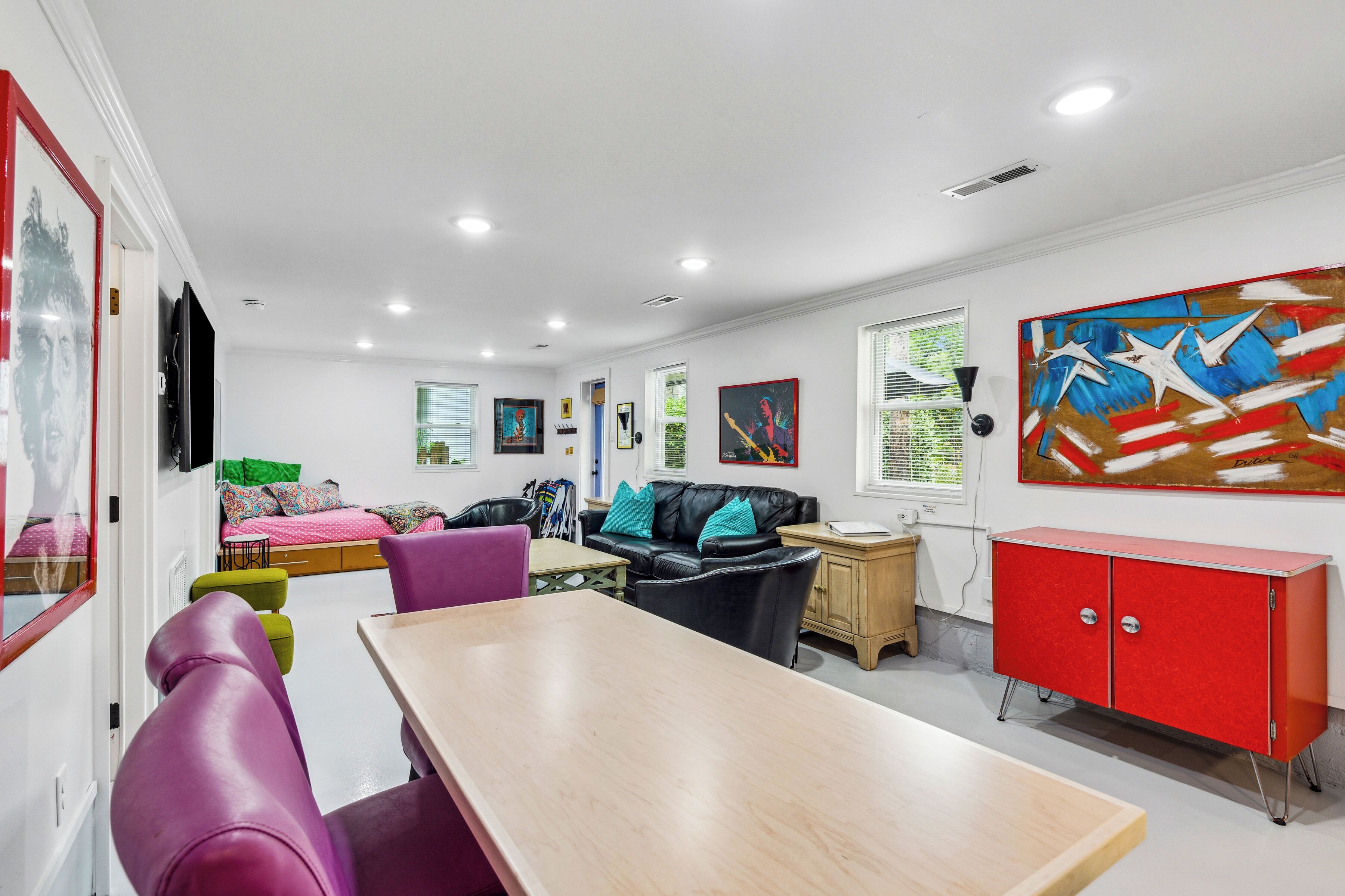 A modern living room with a wooden dining table, a black leather sofa, and a red cabinet.