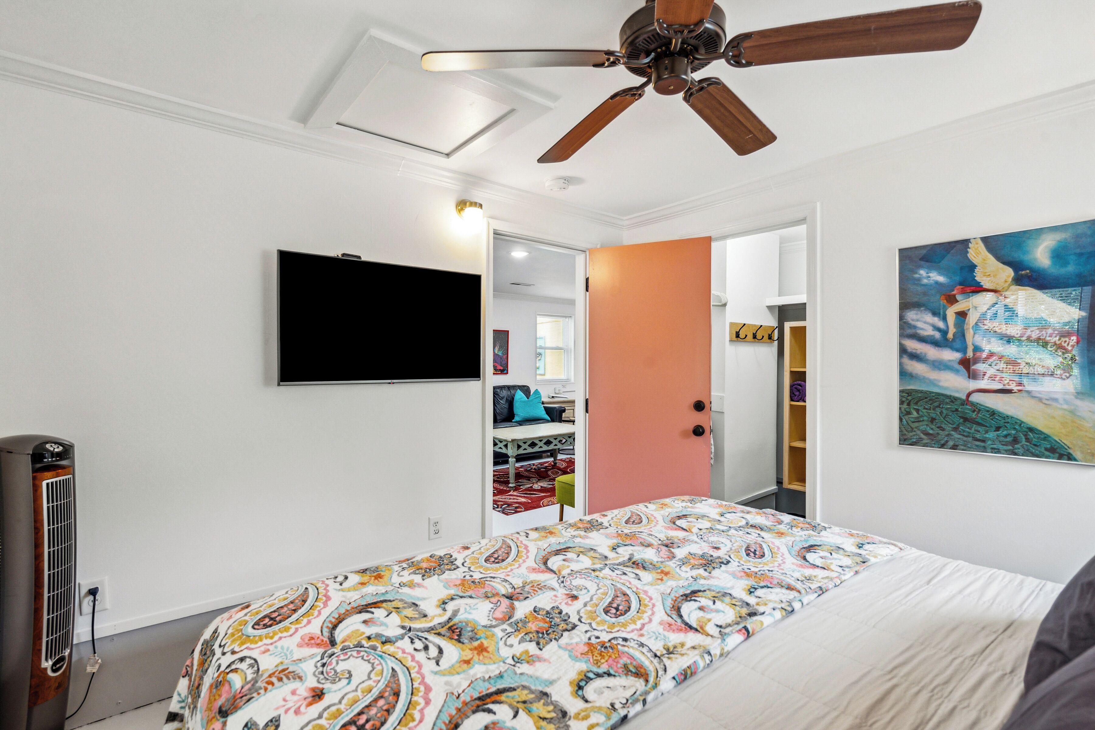 A bedroom with a bed, ceiling fan, TV, and artwork.