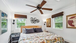 A bedroom with a large bed, a ceiling fan, two bedside tables, and a red rug.