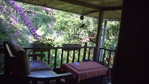 A covered porch with a wooden bench and table, surrounded by lush greenery and purple flowers. - Casa Hospedaje Tingo Maria (Rupa-Rupa)